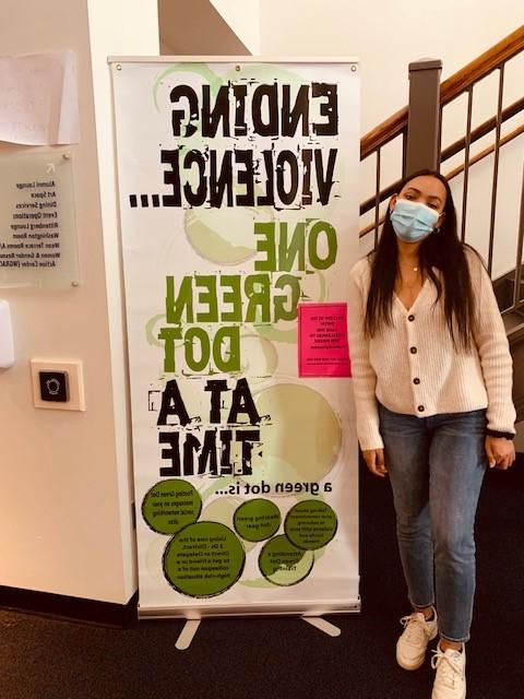 student standing near large green dot sign which reads, ending violence one green dot at a time